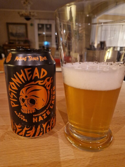 Pistonhead Haze Lager-burk bredvid ett glas fyllt med gyllene öl, fotograferat på en träyta inomhus.