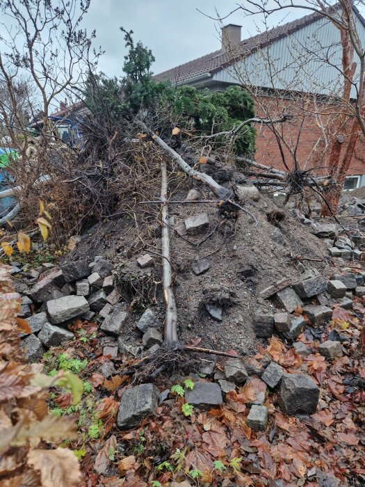 Hög av jord, grenar och stenar intill ett hus i trädgårdsmiljö.