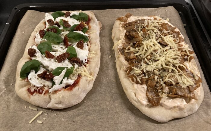 Två pizzor på bakplåtspapper, en med mozzarella, soltorkad tomat och basilika, och en med gyroskött och ost.