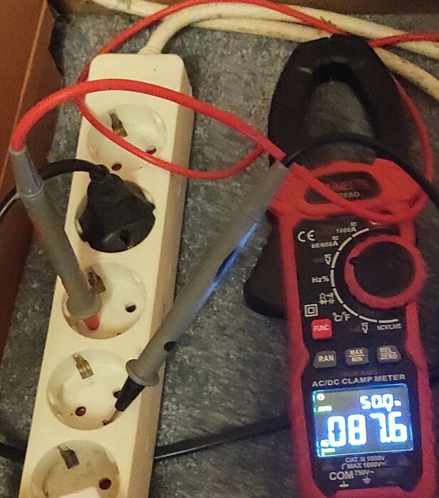 Multimeter mäter spänning på grendosa; en prob ansluten i fas och den andra i skyddsjord. Display visar 87,6 volt.