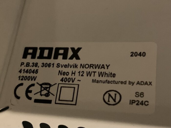 Etikett på Adax-element med 400V-specifikation, märkt "Neo H 12 WT White", 1200W, tillverkat i Norge, innehåller olika säkerhetsmärken och produktinformation.