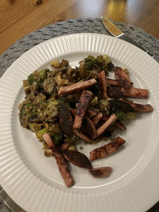 Wok med broccoli, svamp, vitlök, ingefära, cashewnötter och strimlad falukorv på en vit tallrik. Toppad med hoisinsås och sriracha.