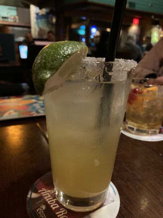 Drink med lime och sugrör i ett glas med saltad kant, serverad på ett underlägg på ett mörkt träbord.