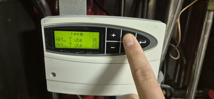 Finger pekar på knapp på digital display av fjärrvärmecentralens styrenhet, visar aktuella temperaturer.