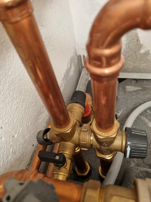 Kopparrör och ventiler som visar kopplingar från en värmepumpinstallation, med fokus på t-koppling och flödesriktning.