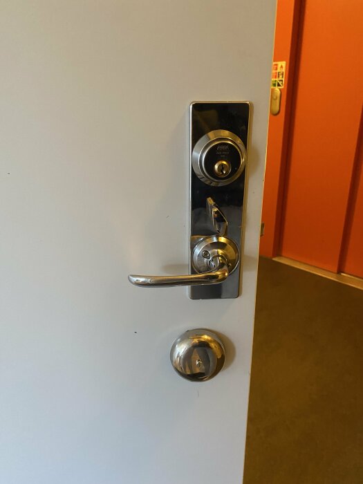 Dörr med metallhandtag och lås från Assa Abloy, frågeställaren undrar vilket lås som ska köpas för byte.