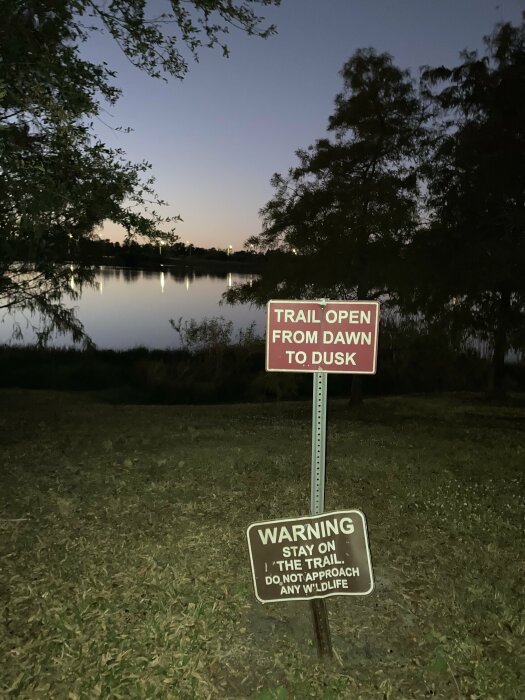 Skyltar vid en sjöpromenad: "Trail open from dawn to dusk" och "Warning: stay on the trail. Do not approach any wildlife.