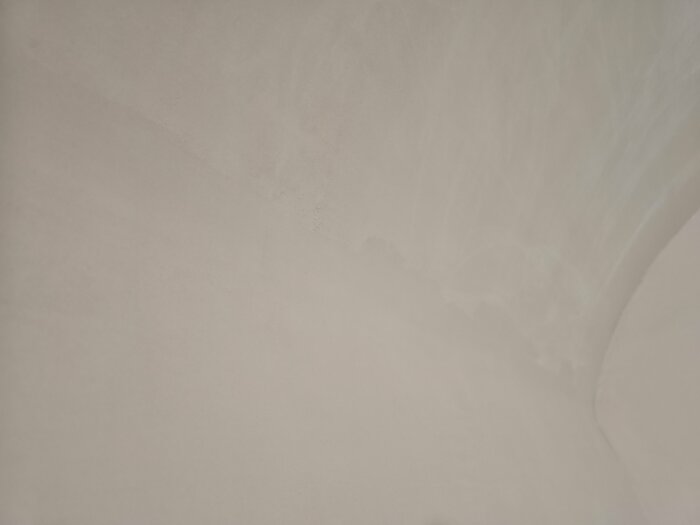 Ojämn yta av microcement på badrumsvägg, med synliga drag och fläckar efter bearbetning, beskrivs som överarbetad och svår att slipa slät.