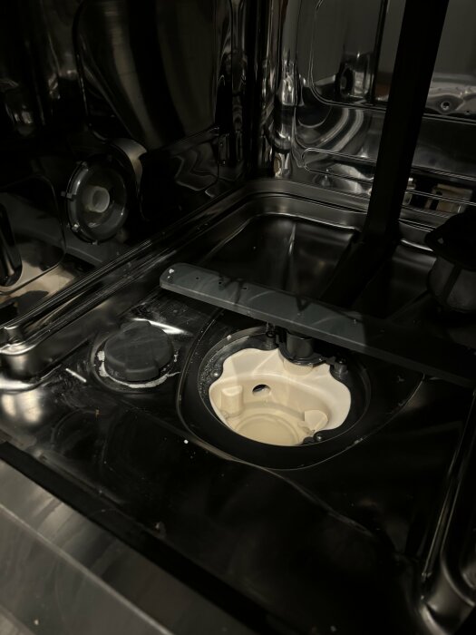 Insidan av en diskmaskin med synligt filter och vattenavlopp.