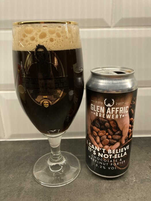 Ett glas mörk porter från Glen Affric Brewery vid sidan av en ölburk med etiketten "I Can't Believe It's Not-Ella, Chocolate & Hazelnut Porter".