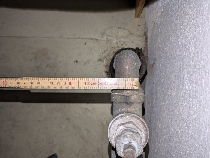 Gammal vattenventil med anslutande rör mot en vägg och ett måttband som mäter diametern, potentiella byten vid renovering.