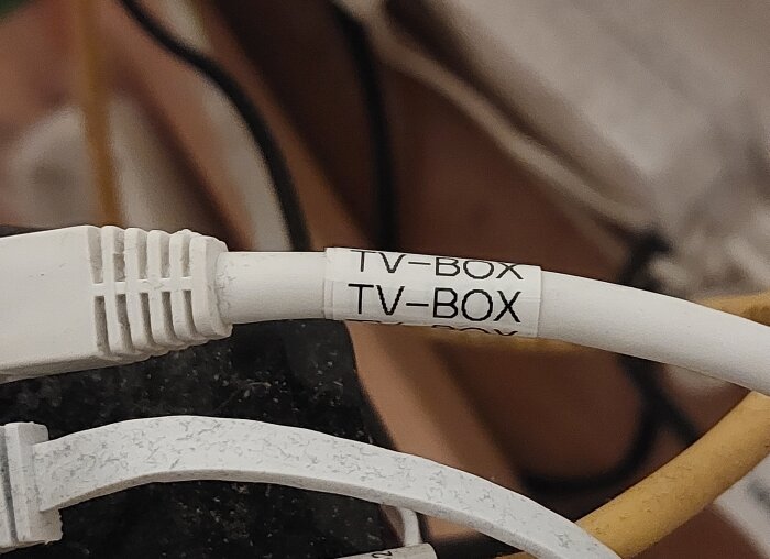 Vit kabel märkt "TV-BOX" med etikett, illustrerar användning av Brother P-touch för kabelmärkning.