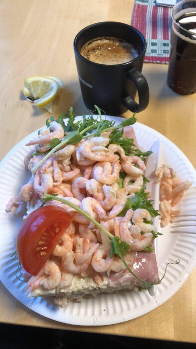 RÀksmörgÄs pÄ papptallrik med kaffemugg och colaglas pÄ bord bredvid en citronskiva.
