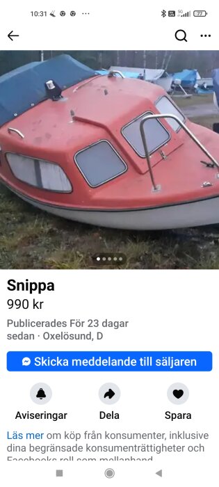 Röd fritidsbåt med styrhytt och två fönster, placerad på gräs. Båten är till salu för 990 kr i Oxelösund.