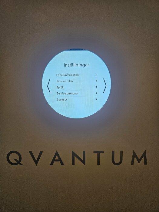 LCD-skärm som visar menyn för inställningar med alternativ som enhetsinformation och språk. Texten "QVANTUM" syns under skärmen.