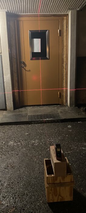 Nyinstallerad provisorisk dörr med mätlinjer i rött ljus för uppmätning av karmen vid byggprojekt, placerad i ett kvällsbelyst utrymme.