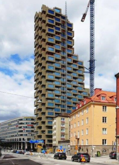 Höghus i Stockholm med ovanlig arkitektur; byggnaden har bruna fasader och oregelbundna fönster, omgiven av andra byggnader och en byggkran.