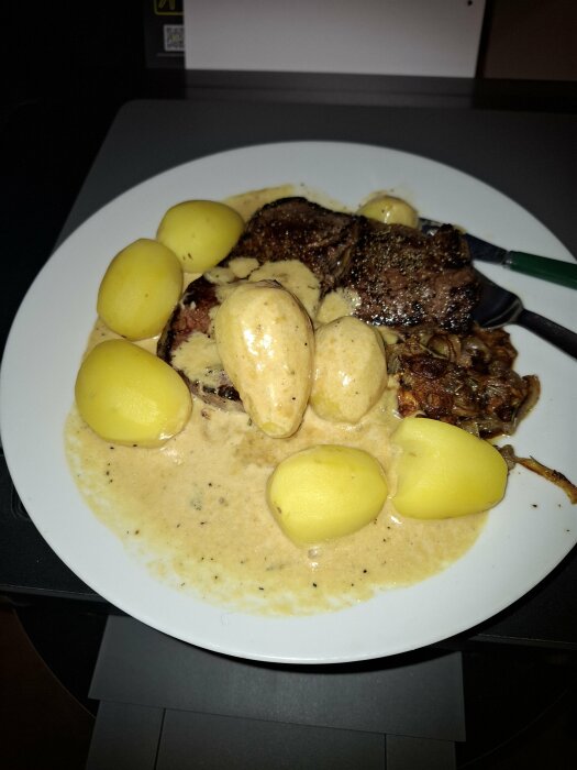 Tallrik med ryggbiff, kokt potatis och gräddsås placerad på en skrivare.