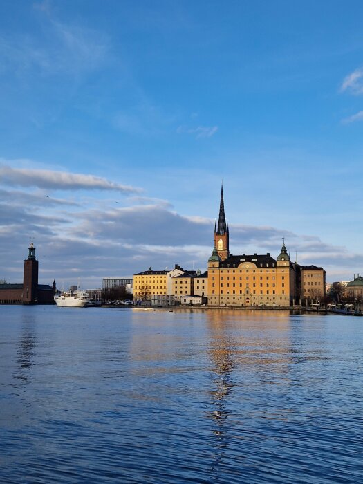 Stadshuset och Riddarholmskyrkan vid vattnet i Stockholm, under en klar blå himmel.