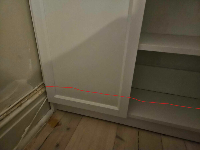 Närbild av nederdelen på en vit bokhylla från IKEA, med en markerad linje vid golvet, som visar potential för renovering med lister och belysning.