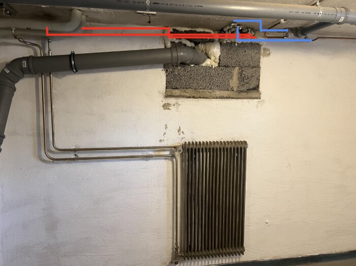 Rörinstallation i källare med synliga ledningar markerade i rött och blått, samt radiator mot vit vägg.