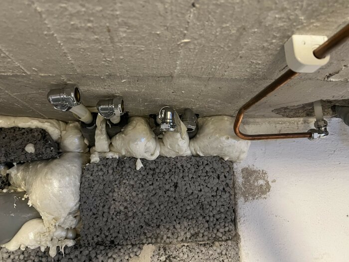 Isolerade rör och ventiler monterade i en vägg fylld med isolerande skum, bredvid en kopparledning som ansluter till vattenburet värmesystem.