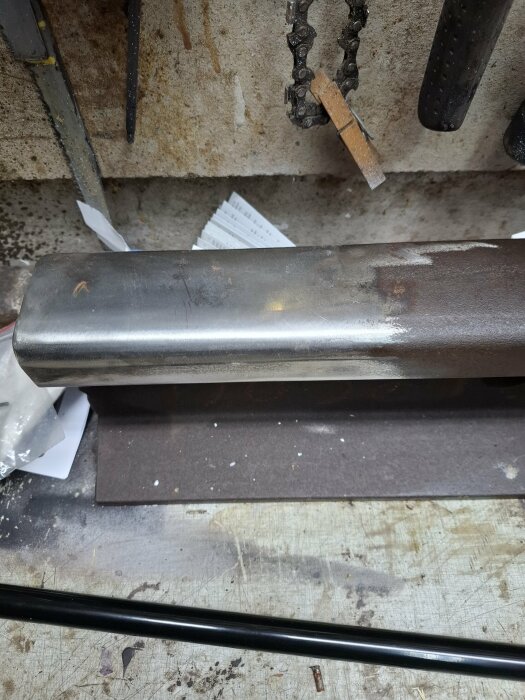 Polerad järnvägsräls på arbetsbänk, delvis slipad och polerad, med verktyg och papper i bakgrunden.