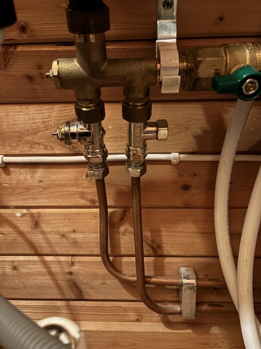 Ventil med kopparrör kopplad till golvvärmefördelare monterad på trävägg.