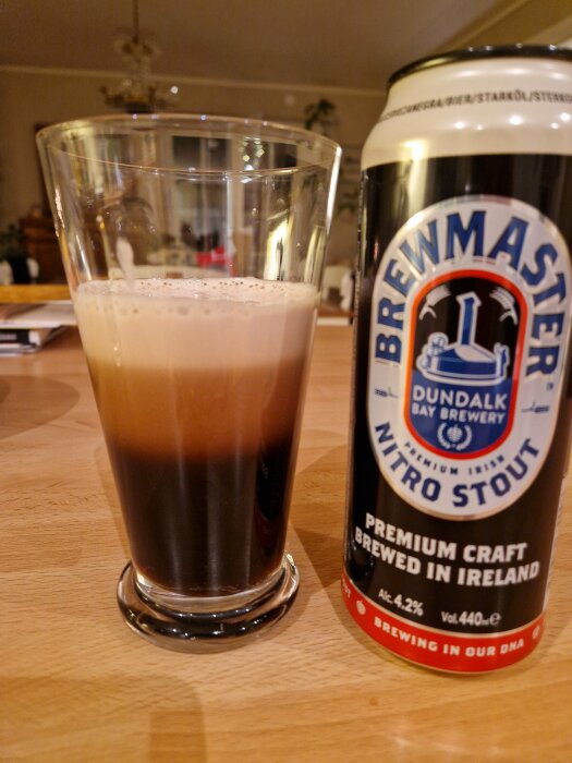 Glas med stoutöl bredvid en Brewmaster Nitro Stout-burk på ett träbord.