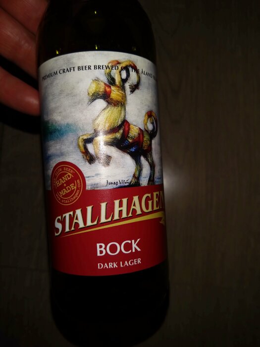 Flaska Stallhagen Bock Dark Lager med etikett som visar en häst, en hand i bakgrunden.