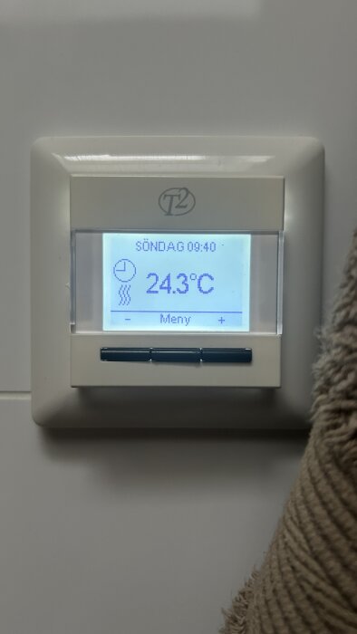 Digital termostat T2 visar 24,3 grader Celsius på en vit vägg.