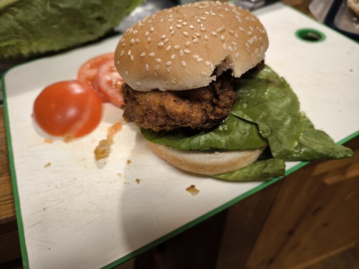 Hemlagad Zingerburgare med krispig kyckling på en sesambulle, serverad med sallad och tomatskivor på en skärbräda.