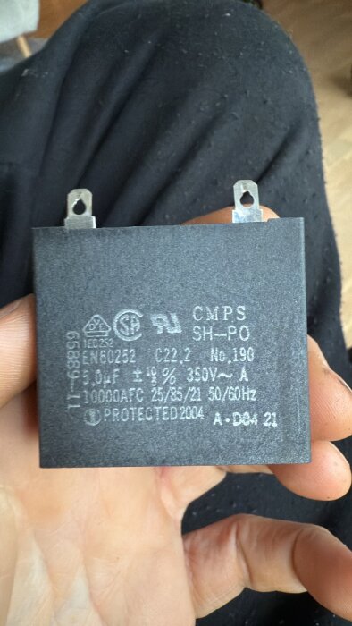 Kondensator CMPS SH-PO 5,0uF 350V ligger i en hand, kopplad till kylskåpsproblem och jordfelsbrytare.