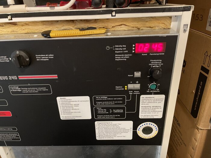 Värmepanna med digital display visar 02 och 45, kontrollknappar och ratt för justering av värmekurva syns. Verktyg placerat ovanpå pannan.