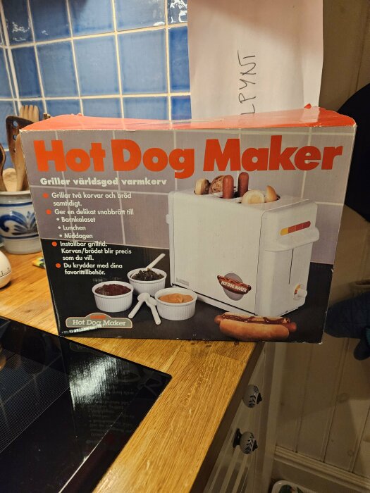 Förpackning av en "Hot Dog Maker" som grillar korvar och bröd samtidigt, med illustration och användningstips synligt på kartongen.