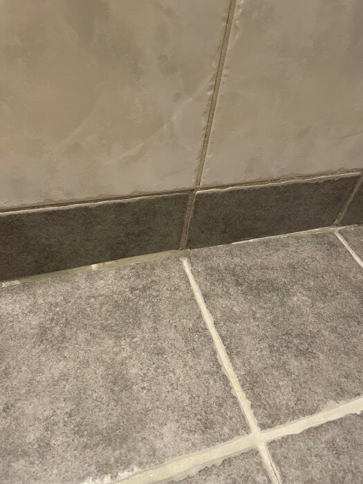 Sliten kakelfog på badrumsgolv där silikon har tagits bort, med några fogar som har börjat lossna.