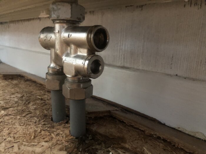 Justerskruv och kopplingar på ett värmeelement mot en plywoodvägg.