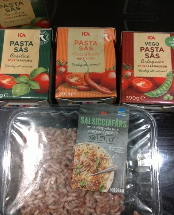 Förpackningar med ICA pastasås och en plastförpackning med salsicciafärs på ett bord, redo för att lagas till middag.