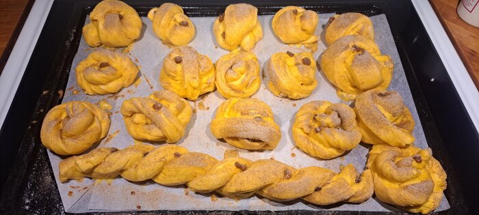 Nygräddade lussekatter och flätor med saffran och russin ligger på ett bakplåtspapper.