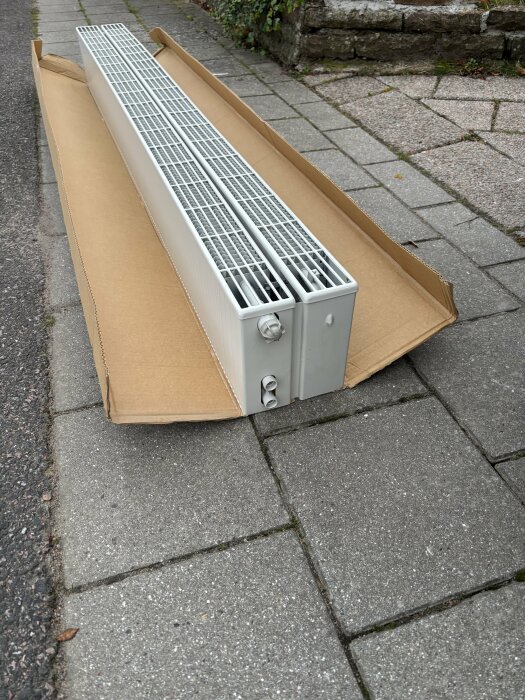 Radiator för vinterträdgård i kartong, liggandes på stenlagd trottoar.