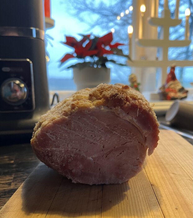 Griljerad julskinka på en skärbräda med juldekorationer och en röd julstjärna i bakgrunden.