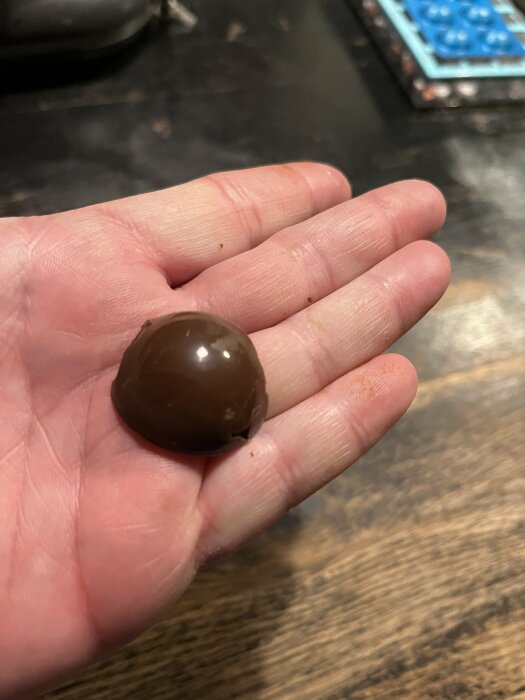 En hand håller en halvcirkelformad chokladpralin, framställd i hemgjord pralinform.