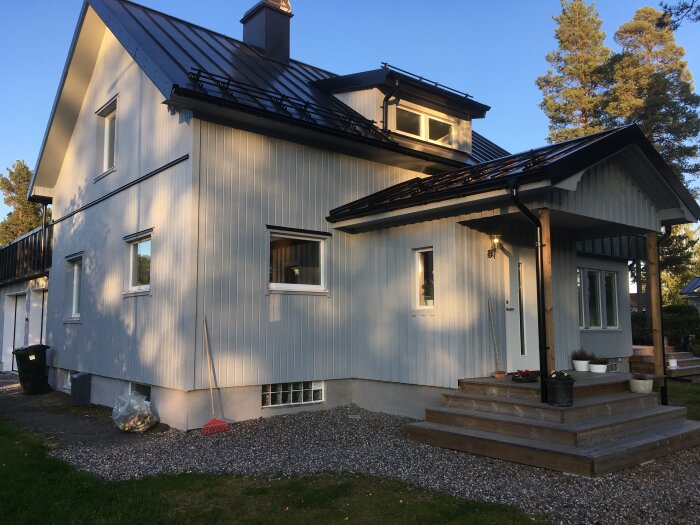 Ett blått hus med svart tak och källare, 1,5 plan. Byggt 1946, renoverat tak med cellplastisolering och plåt. Entré med trappa och blomkrukor.