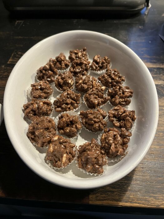 Hemmabakat chokladgodis med puffat ris och musli, arrangerade i knäckformar i en vit skål på ett mörkt bord.