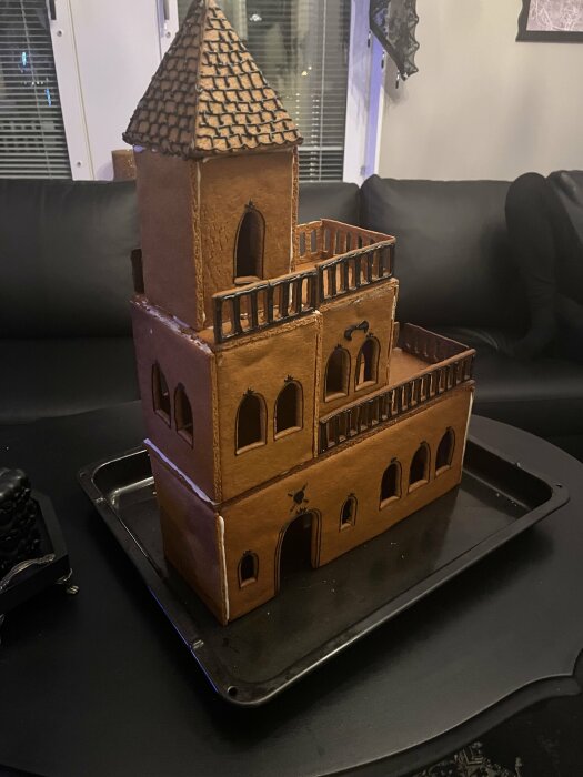 Pepparkakshus i flera våningar med torn och detaljer, placerat på en plåt på ett bord i hemmiljö.