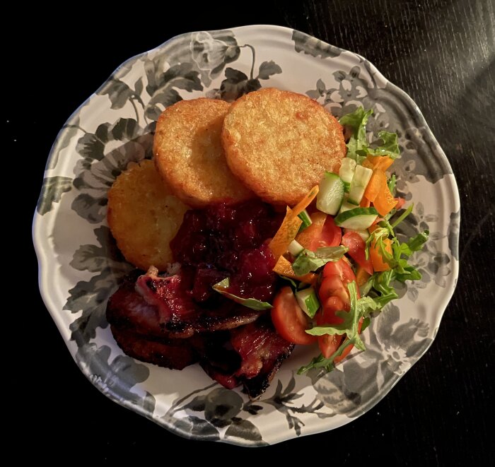 Stekt fläsk och potatisbullar på tallrik med sallad och lingonsylt.