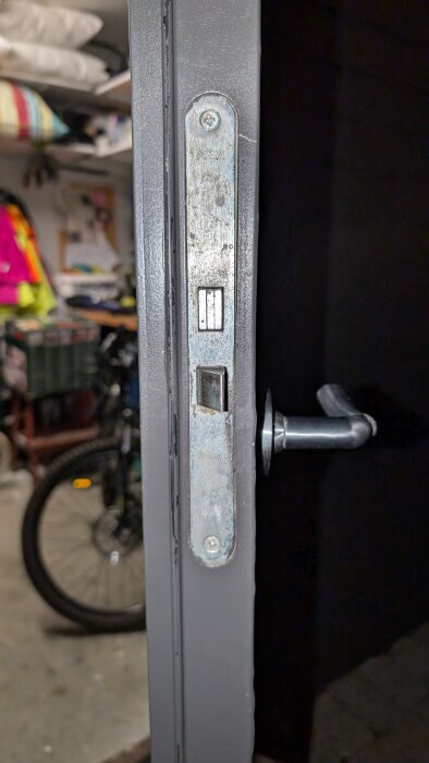 Närbild av dörrkarm med installerat slutbleck för Yale Doorman, omgiven av garageartiklar och cykel i bakgrunden.