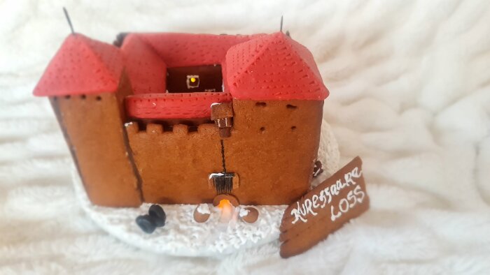 Pepparkaksmodell av Kuressaare slott med röda tak, placerad på vit yta. Skylt med texten "Kuressaare Loss" syns bredvid.