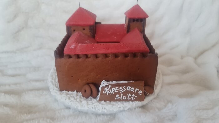 Pepparkaksmodell av Kuressaare slott med röda tak och en skylt med texten "Kuressaare slott", placerad på en vit bakgrund.