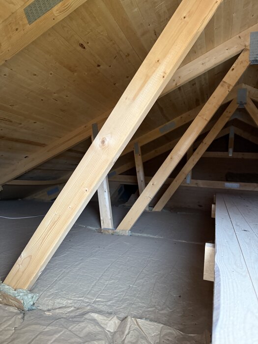Trästolar på vinden i ett hus under renovering, med synliga takstolar och isolering på golvet.